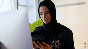 Woman wearing Hijab Abaya using smart mobile cell phone. Beautiful fair skin Middle Eastern female Arab using mobile app, online banking or internet browsing concept
