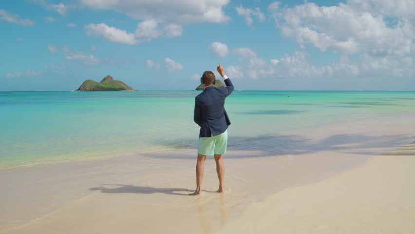 Male tourist overwhelmed with happiness dancing in jacket and beach shorts on white sand admiring the beauty of the vast blue ocean creating scenic horizon. High quality 4k footage Royalty-Free Stock Footage #3448984975