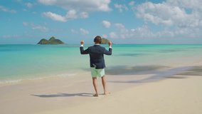 Male tourist overwhelmed with happiness dancing in jacket and beach shorts on white sand admiring the beauty of the vast blue ocean creating scenic horizon. High quality 4k footage - Powered by Shutterstock - Get 15% off with code: PIKWIZARD15