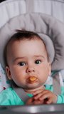 Baby boy nutrition at mealtime. Adorable baby is given food and he waves hands cheerfully and shows tongue. Vertical video.