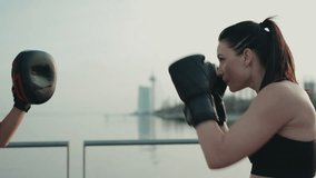 Two athletic women engage in boxing training outdoors. One woman punches while the other holds the pads by a serene waterfront setting. - Powered by Shutterstock - Get 15% off with code: PIKWIZARD15