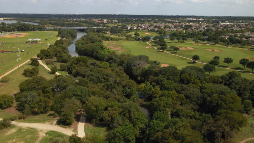 Aerial view of Central Texas community, trails, real estate, neighborhood, park, shot dives from high above trees to low glide on river, drone 4K