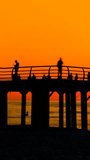 Timelapse, vertical slider video: unrecognizable silhouettes of people are walking fast on the pier against the clear sky over the Black Sea at sunset. Time lapse, summer and tropical concept