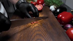 The cook cuts a tomato on a wooden board. Slow motion