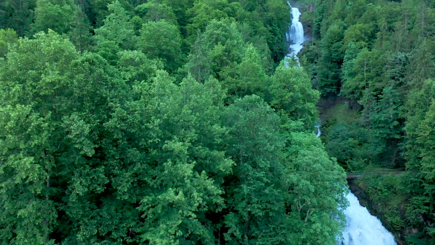Drone flight over a stunning alpine mountain water fall. The water falls cascade down through the alpine forest as the drone flies above the forest landscape.
