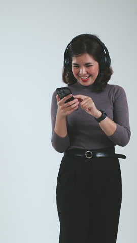 Asian woman listening the music with headphones from mobile phone and dancing isolated on white screen. Vertical