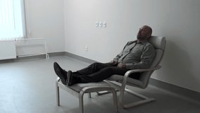 Man is lying in armchair in office. Clip. Man is lying in armchair in empty white room. Man in therapist's chair. Psychological illness