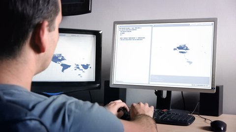 Programmer working with multiple monitors and tracking data on animated world map. Dolly Shot. 