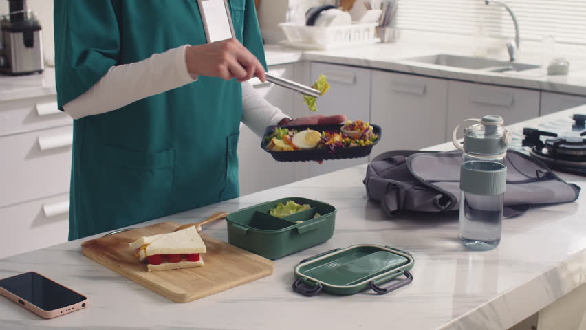 Cropped shot of unrecognizable medical worker in uniform packing lunch box while preparing for work day