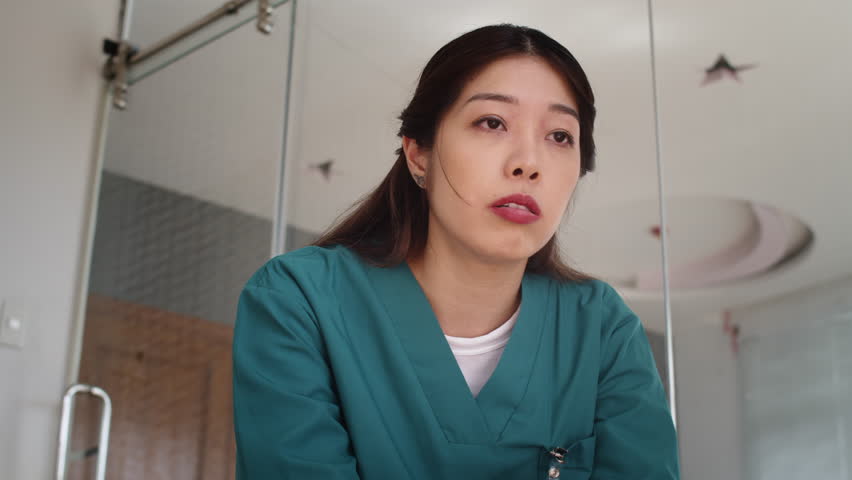 Low angle shot of tired Asian medical worker in uniform suffering from headache after long shift at hospital Royalty-Free Stock Footage #3449235131