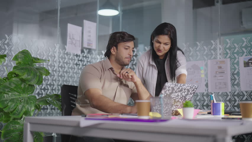 Indian young male aged female colleagues using laptop working serious talking together in office. Senior business woman teaching adult intern instructing helping explain online computer project task Royalty-Free Stock Footage #3449238877