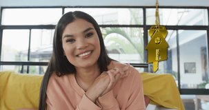 Animation of gold house key and key fob over happy biracial woman at home. House, home, property, ownership and lifestyle concept digitally generated video.