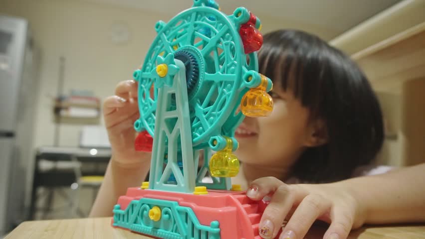 Five-year old Chinese Indonesian girl playing with plastic ferris wheel toy in a living room setting. Static shot, low angle. Indoor.