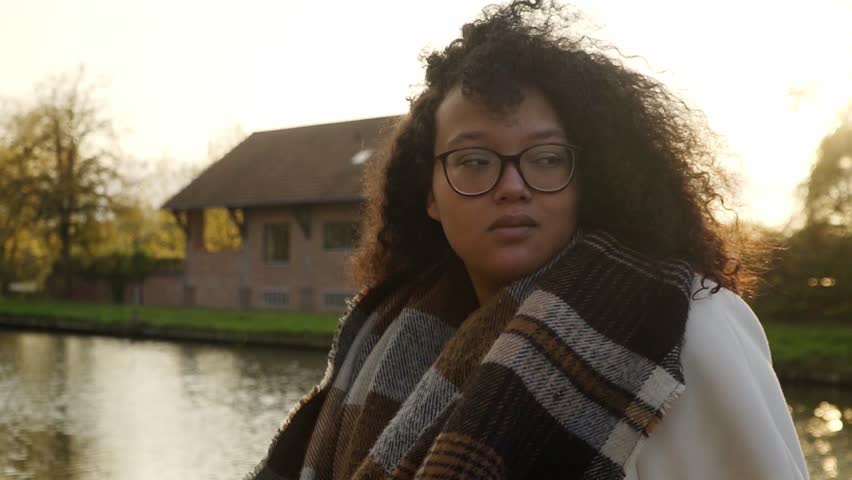 Portrait shot of a beautiful black woman standing in front of the canal during golden hour.