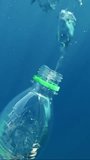 Vertical video, Plastic bottle flowing last bubbles of air and it sinks into blue deep in brightly sun rays, Mediterranean Sea, Slow motion. Plastic pollution of the Ocean