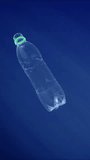 Vertical video, discarded transparent plastic bottle slowly sinking into blue depth of Mediterranean sea in bright sun rays, Slow motion. Concept plastic pollution of the Ocean