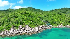 Over emerald forests and turquoise waves, a drone captures the stunning beauty of a tropical island's rocky shoreline from above. Aerial view. Stock footage. Gulf of Thailand. Sea background. 4K.
