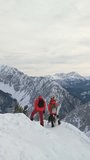 Vertical Aerial drone video of mountaineer couple raise their arms celebrating reaching the top of the mountain
