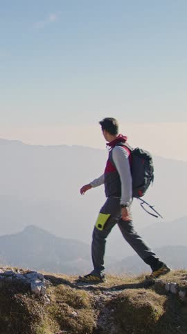 Young couple, hikers giving high five to each other and hugging, looking at a fantastic mountain panorama, pointing in the distance on the bright sunny day, aerial vertical shot.