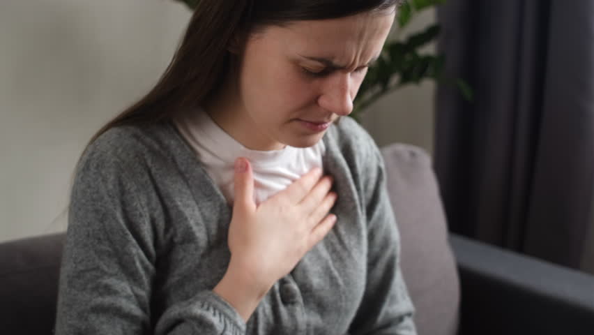 Heart attack threat. Upset young caucasian woman feeling strong ache in chest, writhing in pain, sitting on couch at home. Disease have frequent belching. Healthcare medical and people concept Royalty-Free Stock Footage #3449554673