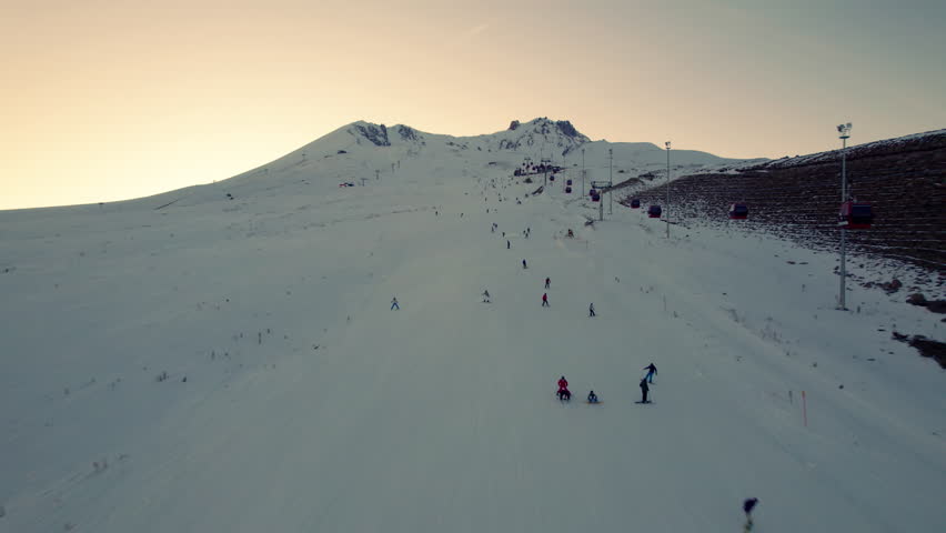 Skiers on snow covered slope of ski resort in the evening. Aerial view. Erciyes Mount, Kayseri province, Turkey