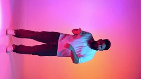 Positive young man with beard dressed casual outfit energetically dancing in neon light against vibrant gradient studio background. Concept of human emotions, self-expression, beauty and fashion. Ad