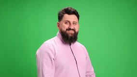 Young brunette man with beard in smart casual outfit confidently looking at camera against vibrant green studio background. Concept of human emotions, self-expression, business fashion. Ad