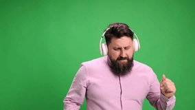 Energetic, emotional man singing while listening his favorite music playlist against vibrant green studio background. Concept of positive human emotions, self-expression, rest, hobbies, leisure time.