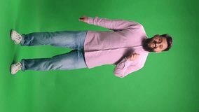 Music enjoyment. Joyful bearded man in pink shirt and jeans dancing against vibrant green studio background. Concept of human emotions, hobbies, leisure time, Friday mood. Vertical orientation