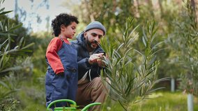 A heartwarming moment as a bearded father explains the intricacies of plant life to his curious young son in a verdant garden setting, while planting a tree together - Powered by Shutterstock - Get 15% off with code: PIKWIZARD15