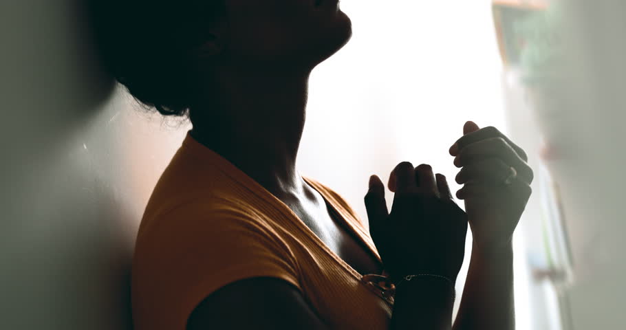 One spiritual young black woman putting hands on chest feeling GRATITUDE. Earnest African American person feeling heartfelt contemplation leaning on wall