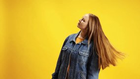 Portrait of young positive woman in denim jacket dancing raised hands up of joy and happiness against yellow studio background. Concept of beauty and fashion, self-expression, human emotions.