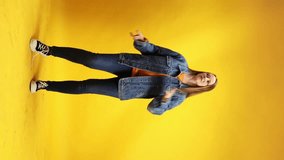 Cheerful young woman with red hair and freckles dressed retro style outfit dancing against yellow studio background. Concept of human emotions, self-expression, hobby, relax. Vertical orientation Ad
