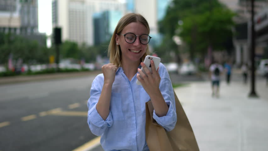 Happy excited young woman receiving discount for shopping while checking email box on mobile calling for sharing success with friend while walking in urban setting down street Royalty-Free Stock Footage #34497178