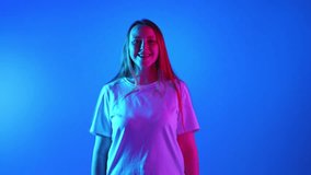 Woman with freckles and ginger hair laughing looking at camera and clenching fists against gradient blue studio background in neon light. Concept of beauty, fashion, self-expression, human emotions.