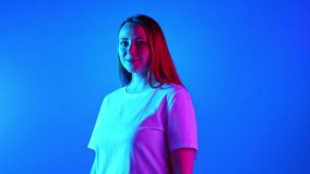 Young and beautiful woman with red hair and freckles looking at camera and moving in neon light against gradient studio background. Concept of beauty and fashion, self-expression, human emotions. Ad