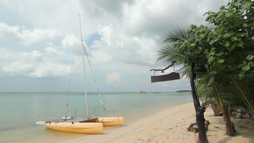 Yellow recreational catamaran boat at a remote, private island beach, cloudy day, no people.