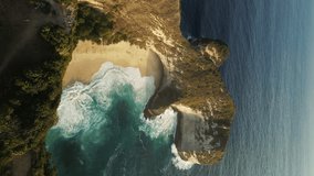 Vertical Video. Drone Shot of the T-Rex Cliff at Kelingking Beach with Deep Ocean Waves Around. Must-Visit Tourist Destination. Aerial View of Kelingking Beach at Sunset on Nusa Penida Island, Bali