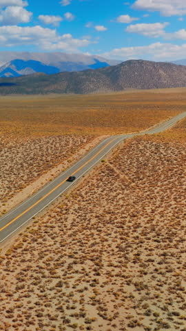 Lonely black car on the road to Nevada, USA. Beautiful sight of desert contrasting with blue skies. Mountains at backdrop. Vertical video.