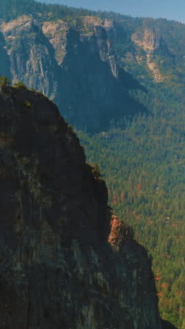 Craggy steep cliffs of Yosemite National Park, California, USA on sunny day. Rare pine trees growing on tops of mountains and thick woods at the foot. Top view. Vertical video.