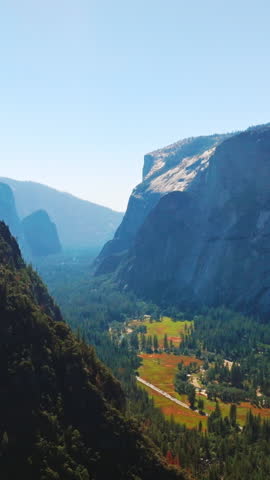 Green sunny valley among the cliff rocks of Yosemite National Park, California, United States. Aerial view at backdrop of clear skies. Vertical video.
