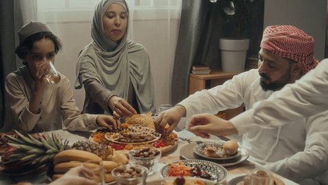 Handheld footage of muslim family members all taking nuts and dried fruits and enjoying then while speaking over festive table on Eid al-Fitr celebration at home Stock Video