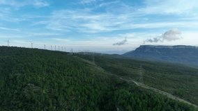 Aerial drone forward flying over high voltage electric pylons with wind farm and mountain in background, Trucafort, Pradell de La Teixeta, Tarragona in Spain. Prores codec