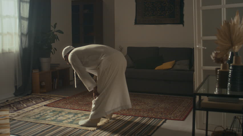 Rear wide footage of unidentified religious man in white cap and thawb making ruku and taking sujud position while expressing gratitude to Allah on prayer mat at home Royalty-Free Stock Footage #3449810455