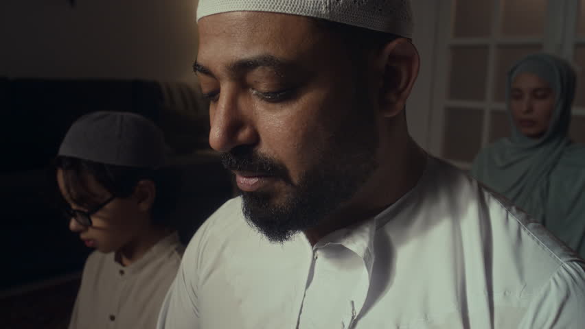 Closeup lowkey shot of religious muslim man quietly reciting Koran and his wife and son listening to it during namaz at home Royalty-Free Stock Footage #3449816007