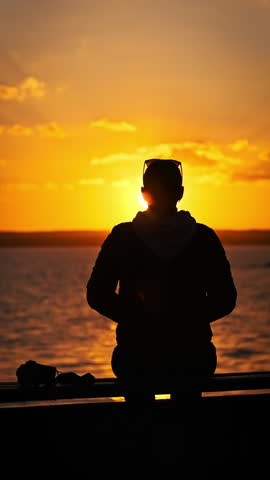 Vertical silhouette of young woman raises hands up against sunset, slow motion. Back view of young girl enjoying life in nature and looking at setting sun. Concept freedom, happiness, mental wellness