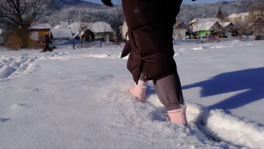 A girl in pink boots walks through the snow. Feet close-up walking in the snow. Walking in the snow slow motion.
