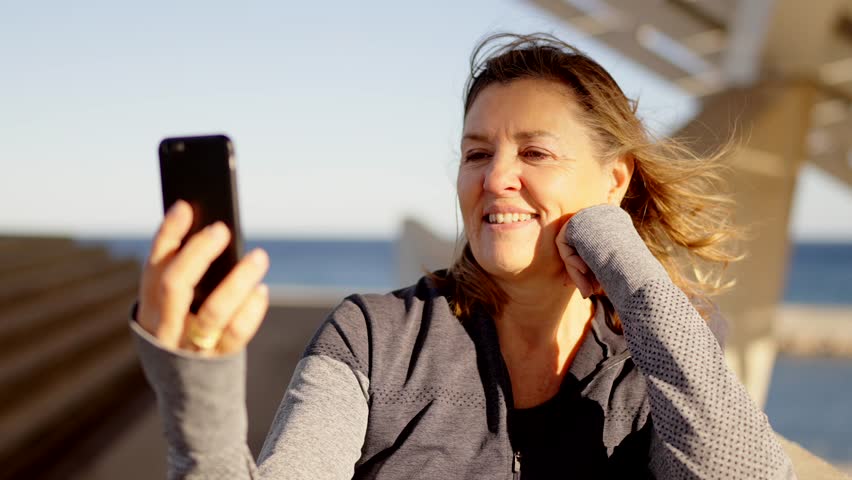 Video of a mature sportive woman during a video call using the mobile outdoors next to the sea Royalty-Free Stock Footage #3449853673