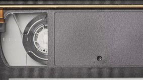 VHS cassette is played inside a VCR tape recorder, top view. Videotape reels rotate. Videocassette with empty blank tag is starting playback. Old video recorder inside close-up. Playing vintage movie - Powered by Shutterstock - Get 15% off with code: PIKWIZARD15