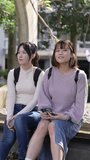 Slow-motion vertical video of two young Taiwanese female college students sitting on a bench and talking happily on a university campus in Taipei, Taiwan